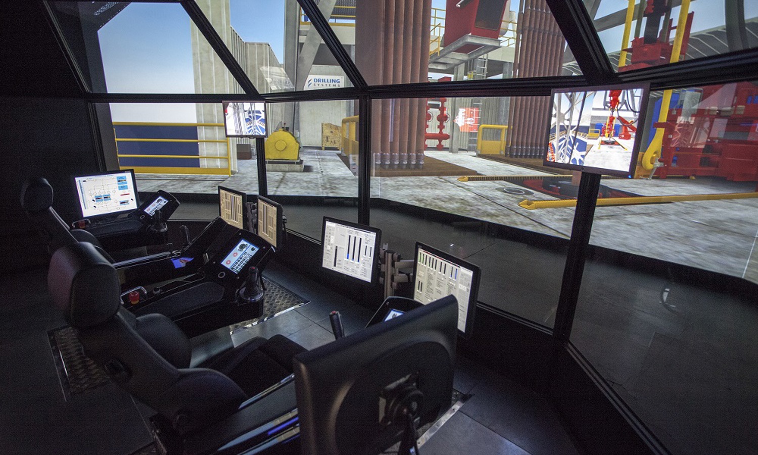 Interior view of a control room with multiple monitors and chairs, featuring screens displaying data and a simulated industrial environment.