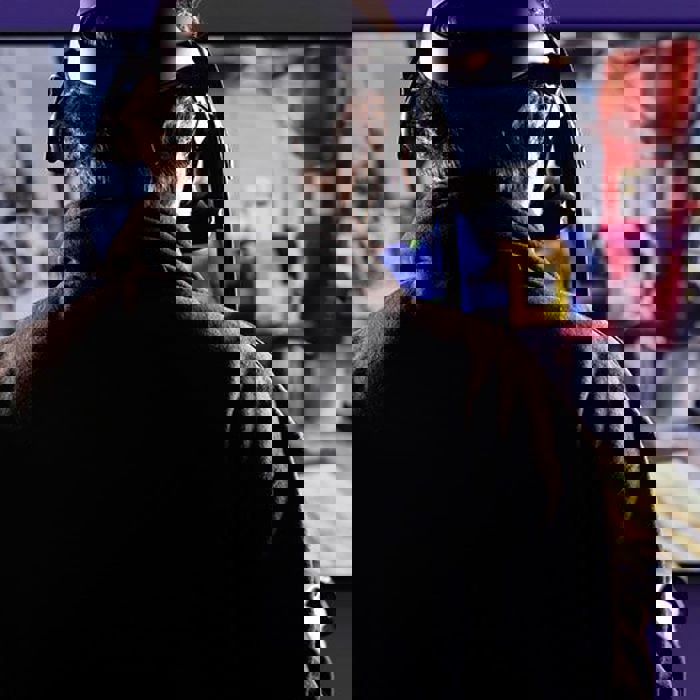 Person wearing a VR headset and holding controllers, engaging with a virtual reality experience. A screen in the background displays a colorful and dynamic scene.