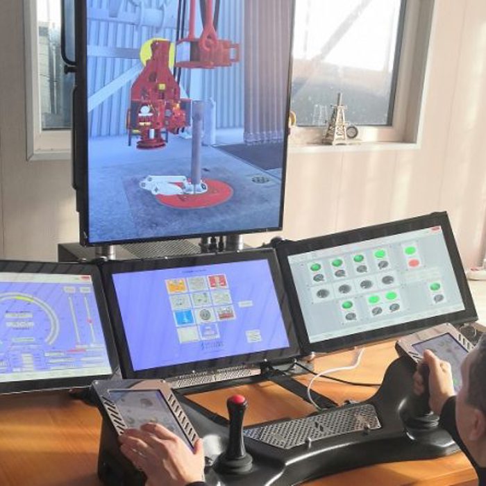 A person operates a remote-controlled machine using multiple monitors and joysticks. The screens display various control interfaces and a live video feed from the machine's location.