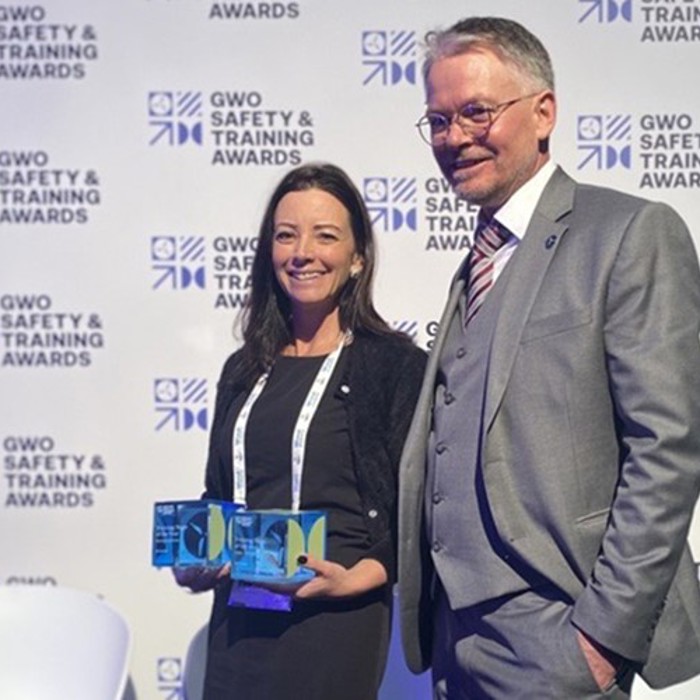 Two individuals stand together at the GWO Safety & Training Awards event. The woman holds two awards, and both are smiling. The backdrop displays the event's logo repeatedly.