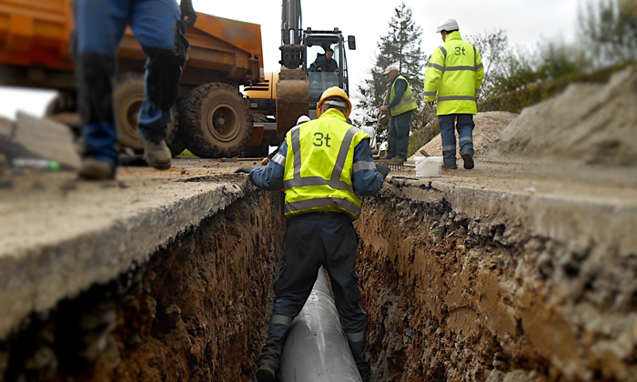 Men wearing yellow high vis jackets laying pipework in a street trench