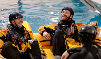 People wearing protective suits and helmets sit in an inflatable raft in a pool, honing their skills during a training exercise.