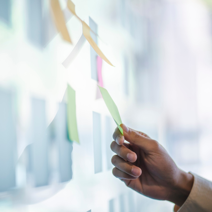 A hand methodically arranges colorful sticky notes on a glass surface, as if setting the stage for a creative training session.
