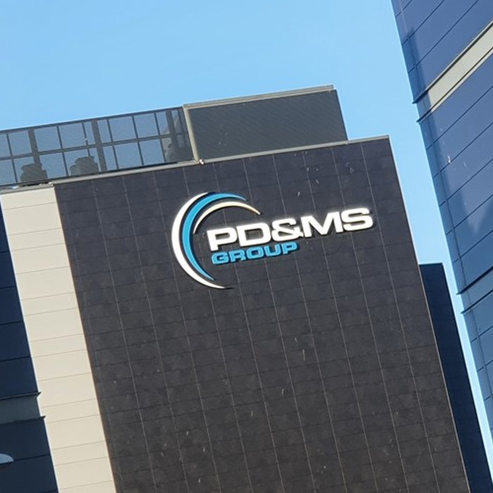The exterior of a modern building with the logo and name "PD&MS Group" displayed on the facade against a blue sky.