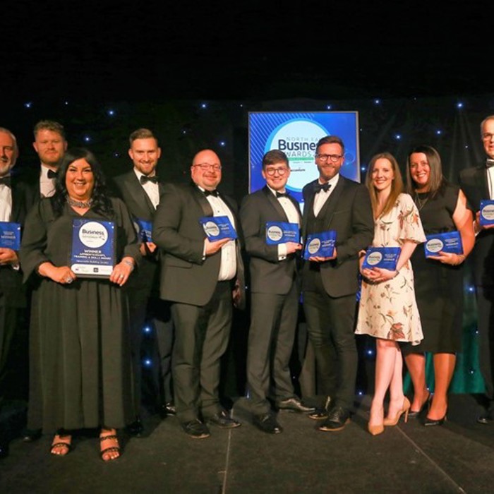 A group of people in formal attire holding awards, standing in front of a banner that reads "Business Awards.