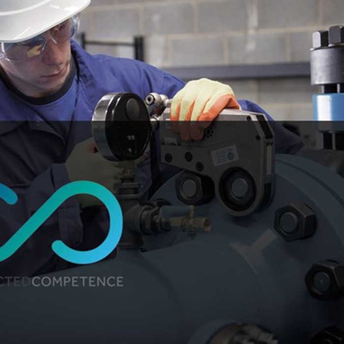 A worker in protective gear operates machinery in an industrial setting, with the Connected Competence logo and text at the forefront.