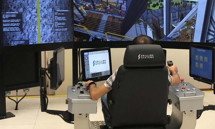 A person operates a high-tech drilling simulation system with multiple screens and control panels, likely used for training or testing purposes.