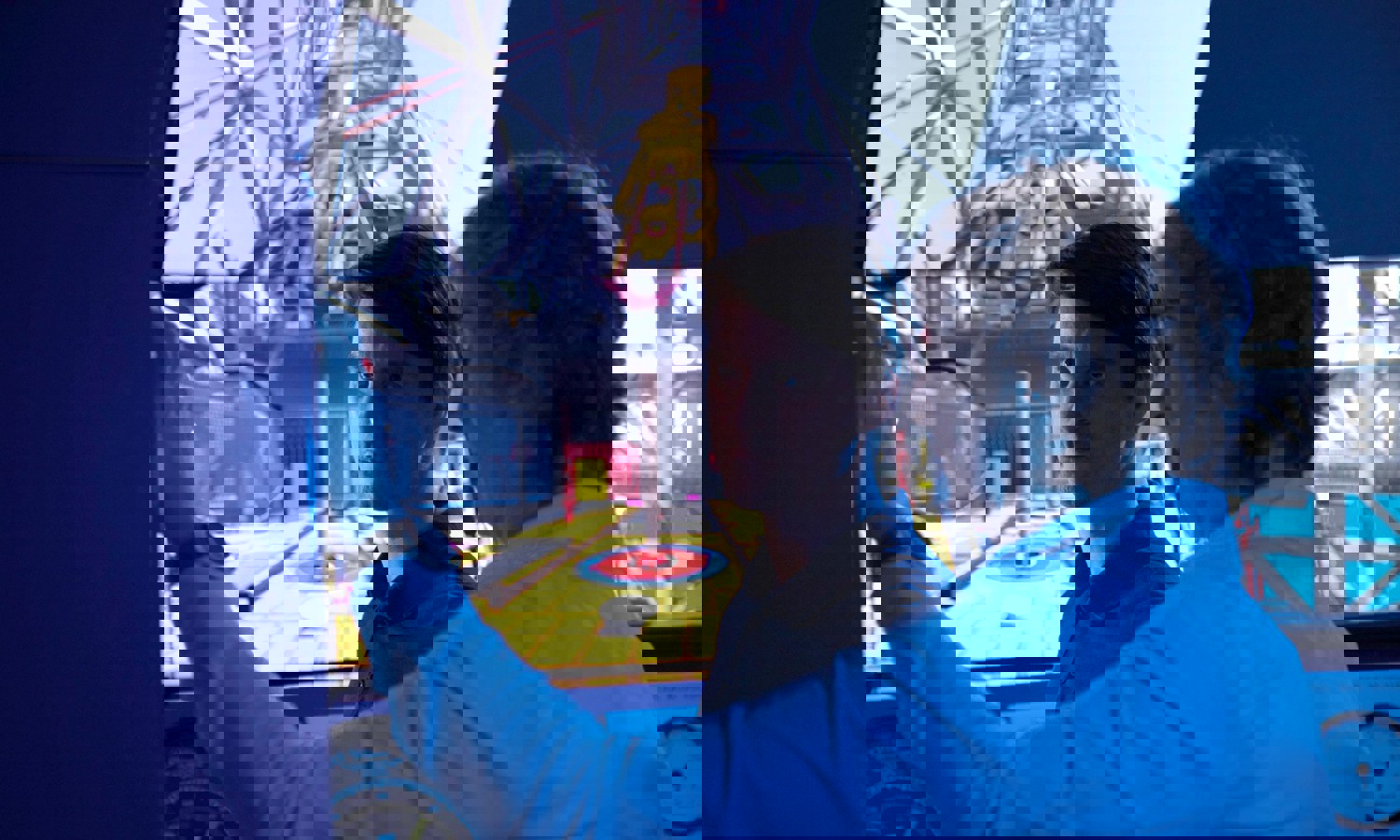 Two men in a control room operate a simulator with a large screen displaying the interior of an industrial setting. One is pointing while the other observes intently.