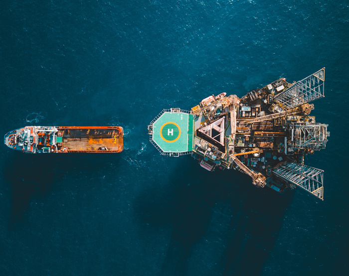 Aerial view of an offshore oil rig with a helipad in the ocean, adjacent to a cargo ship.