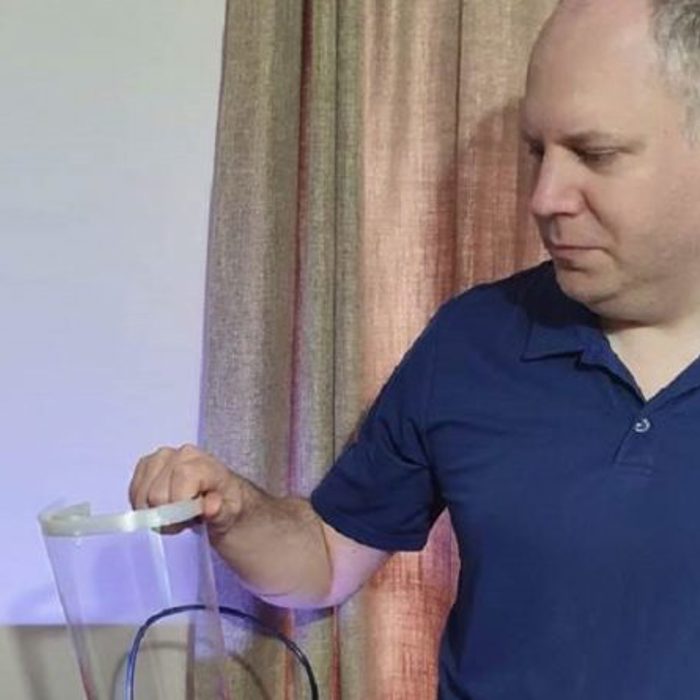 A man in a blue polo shirt looks at a transparent object with a handle against a beige curtain background.